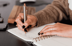 close up of person's hands writing in a notebook.