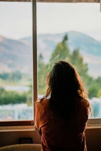 Woman sitting thoughtfully by a window with soft natural light, representing the quiet questions many women have after experiencing sexual assault or rape