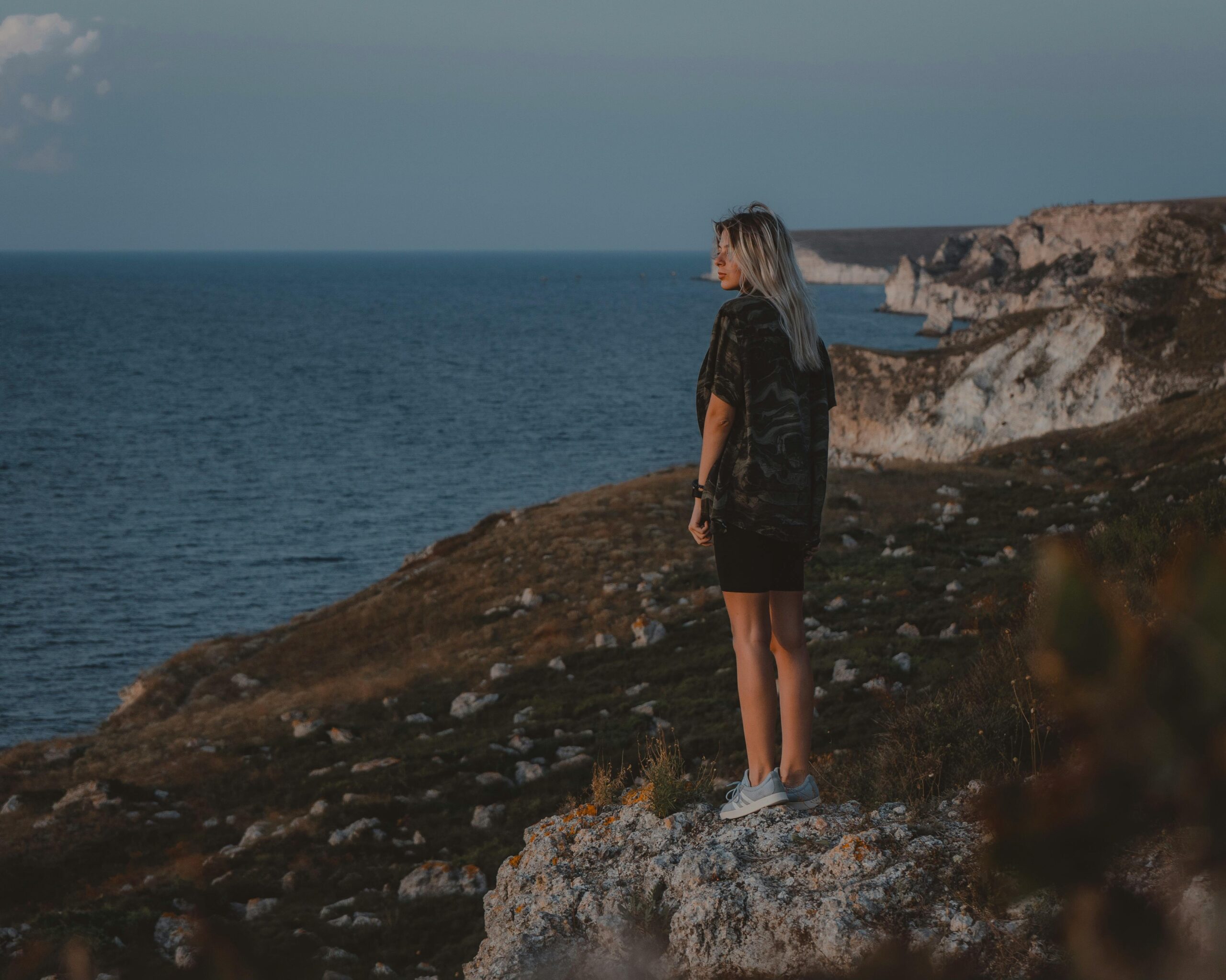 A woman standing calmly and confidently in nature, looking into the distance with quiet strength.<br />
