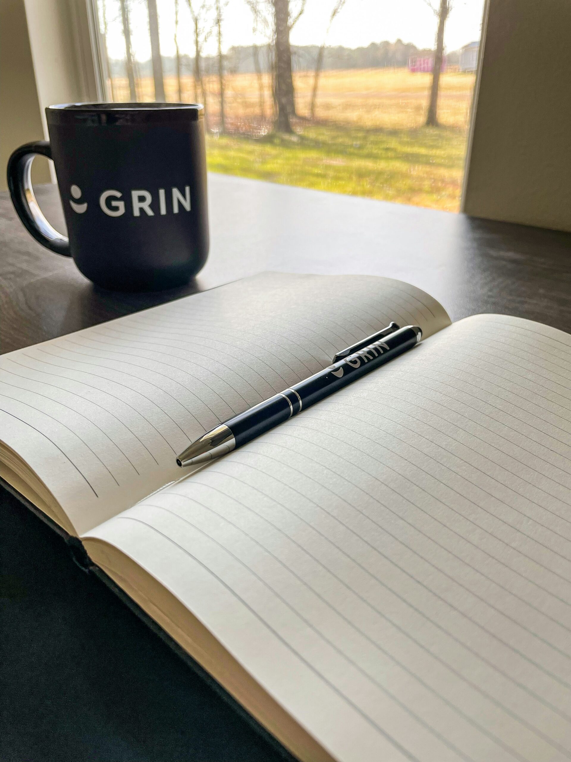 journal, pen and coffee cup on windowsill with a view out to the countryside.